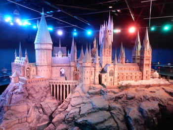 A model castle with several turrets and spires, set upon a rocky mound, under colour lighting